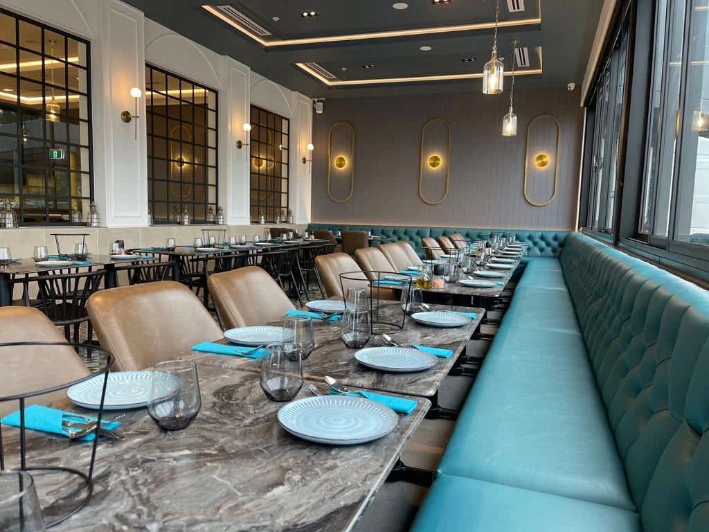 Hospitality dining room with teal tufted banquette seating, marble tables and warm pendant lighting